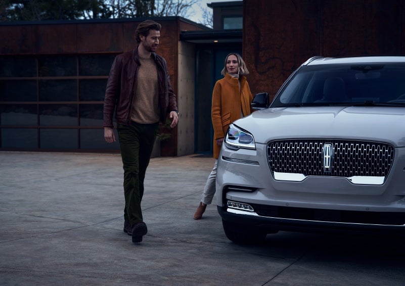 A man and a woman approaching a 2024 Lincoln Aviator® SUV, which illuminates certain lights when they are close | Bondy's Lincoln in Dothan AL