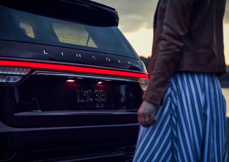 A person is shown near the rear of a 2024 Lincoln Aviator® SUV as the Lincoln Embrace illuminates the rear lights | Bondy's Lincoln in Dothan AL