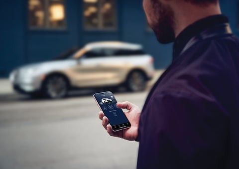 A person is shown interacting with a smartphone to connect to a Lincoln vehicle across the street. | Bondy's Lincoln in Dothan AL