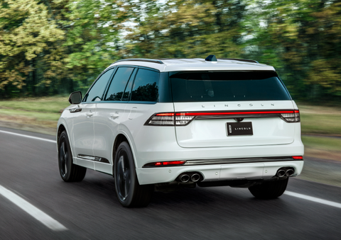 A white 2025 Lincoln Aviator® SUV is being driven away down a road lined with colorful trees. | Bondy's Lincoln in Dothan AL