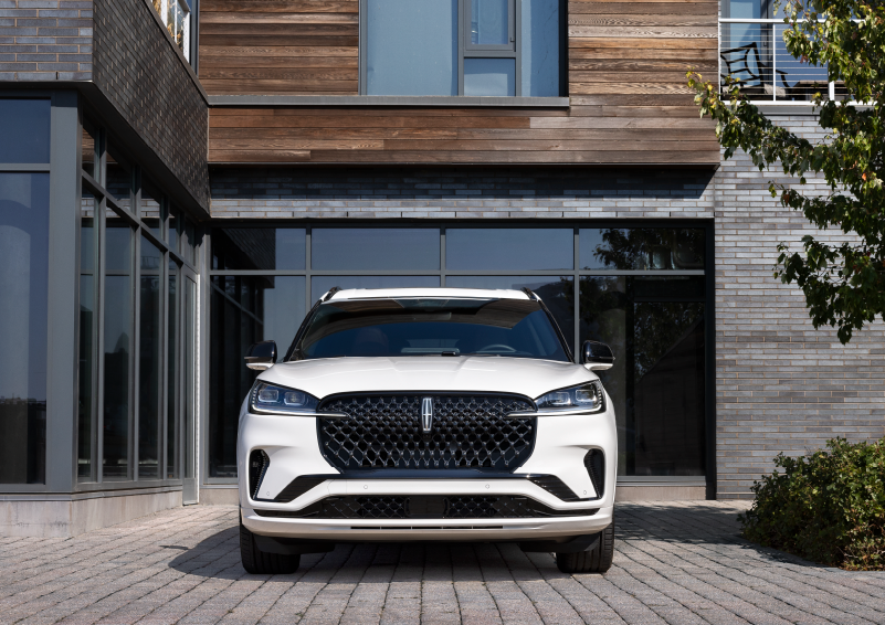 A white 2025 Lincoln Aviator® SUV is shown parked outside a modern building with gray brick and wood accents. | Bondy's Lincoln in Dothan AL