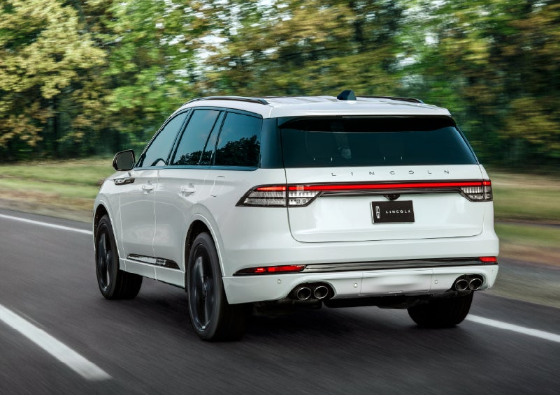 A white 2026 Lincoln Aviator® SUV is being driven away down a road lined with colorful trees. | Bondy's Lincoln in Dothan AL