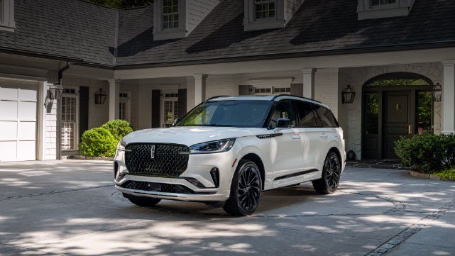 A white 2026 Lincoln Aviator® SUV is parked in the driveway of a luxury home. | Bondy's Lincoln in Dothan AL