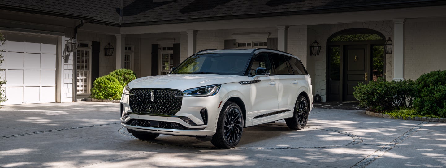 A white 2026 Lincoln Aviator® SUV is parked in the driveway of a luxury home. | Bondy's Lincoln in Dothan AL